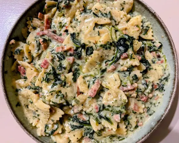 Pyszny makaron farfalle ze szpinakiem i kawałkami boczku w kremowym sosie.
