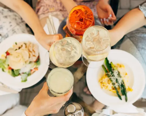 Vänner skålar med drinkar och njuter av en härlig milano mat-upplevelse med sallad och pasta med sparris.