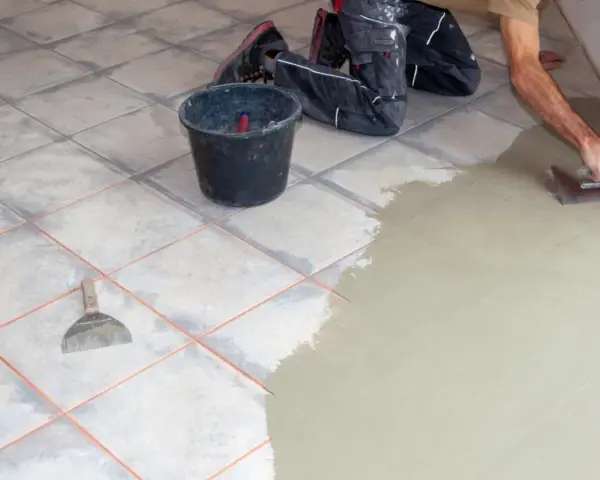 Hand verputzt Fliesen mit Spachtel und Mörtel. Ein Eimer und Werkzeug liegen bereit.