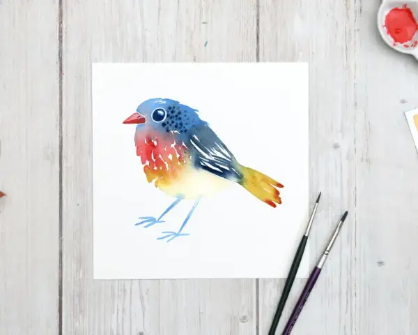 Un charmant dessin oiseau aquarelle aux couleurs vives, posé sur du papier blanc. Des feuilles d'automne et du matériel de peinture complètent la scène.