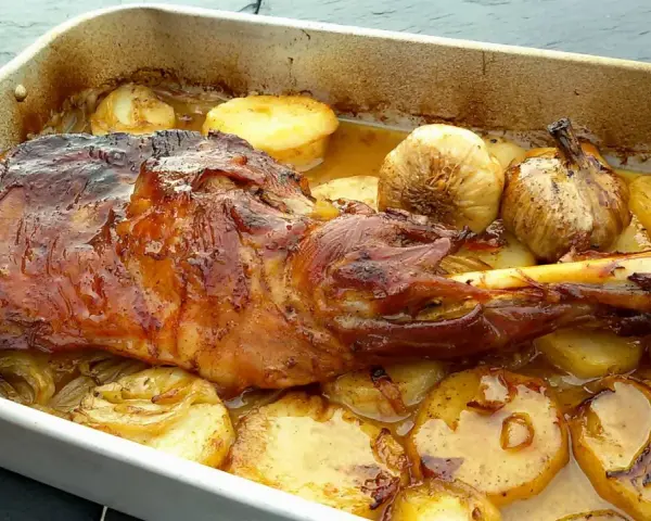 Chuletas de cordero asadas con patatas y ajos en una bandeja.