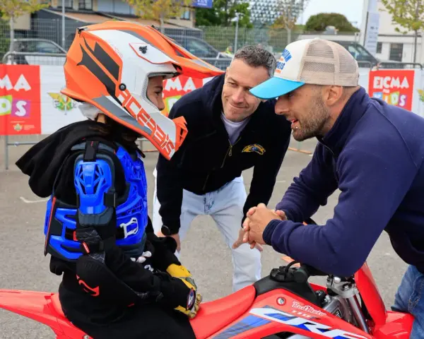 Giovane motociclista donna con casco e protezioni, ascolta i consigli di due uomini.