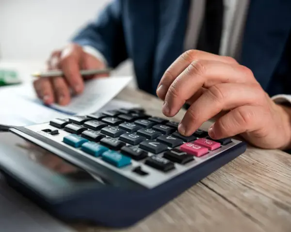 Man con traje calculando en calculadora. Los suplidos llevan IVA, un detalle importante en la contabilidad.