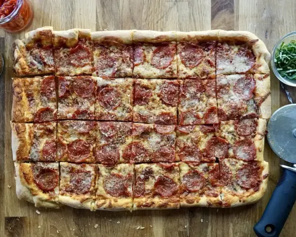 Domowa pizza na blachę z pepperoni, posypana parmezanem. Idealna na rodzinne spotkanie.