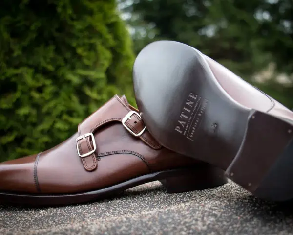 Eleganckie brązowe buty z podwójnymi klamrami, wykonane z wysokiej jakości kruponu. Widoczna podeszwa z logo marki.