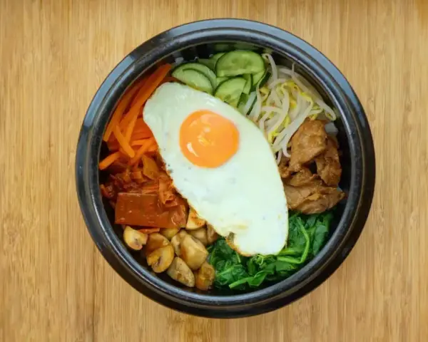 Apetyczne koreańskie jedzenie: miska bibimbap z jajkiem sadzonym, warzywami i mięsem na drewnianym tle.