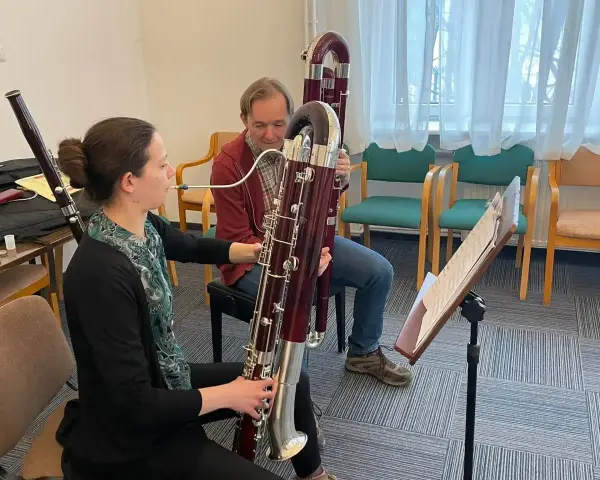 Kobieta i mężczyzna ćwiczą grę na fagotach. Jaki to instrument? Dwa duże, drewniane instrumenty dęte drewniane, fagot, są w centrum uwagi.