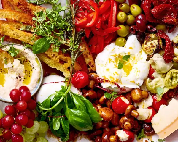 Eine Platte mit geilen Snacks: Hummus, Burrata, Trauben, Brot, Oliven, Pilze, Tomaten und Käse.