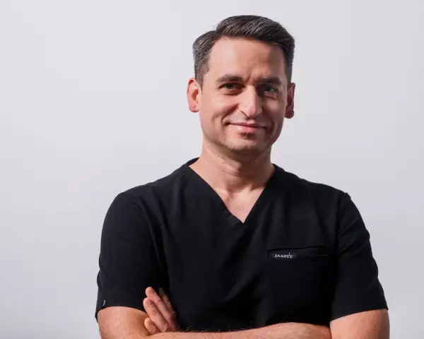 Portret mężczyzny w czarnym scrubie medycznym, ze skrzyżowanymi rękami.