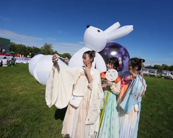 Trzy dziewczyny w tradycyjnych strojach robią sobie selfie na tle dmuchanego królika i księżyca. Królik to chiński znak zodiaku 2012.