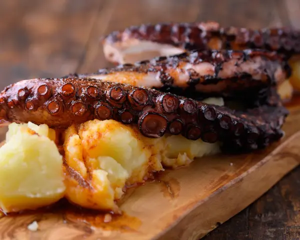 Pulpo tierno con patatas cocidas y espolvoreado con pimentón, servido en tabla de madera.