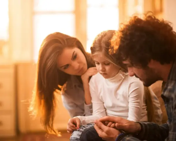 Eltern psychisch kranker Kinder spenden Trost. Ein Vater hält die Hände seiner Tochter, während die Mutter sie zärtlich berührt.
