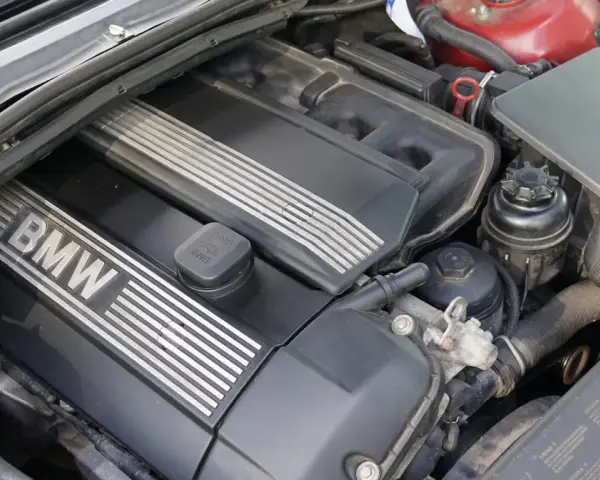 Silniki BMW E46, widok z góry na czarną pokrywę z napisem BMW i srebrnymi paskami. Widać też elementy układu dolotowego i zbiorniczek płynu.