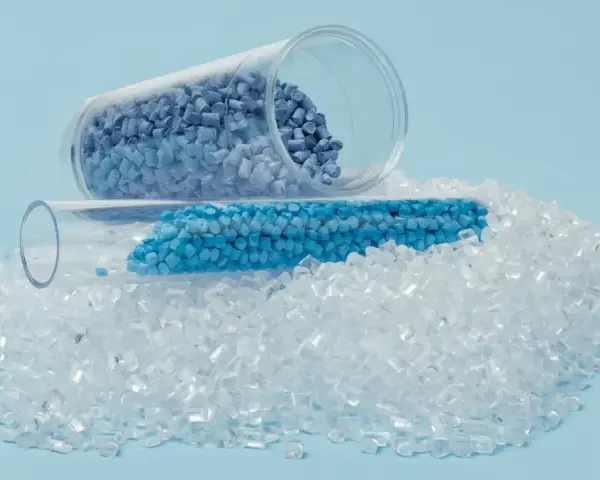 Granulat plastiku w probówkach i rozsypany na jasnoniebieskim tle.