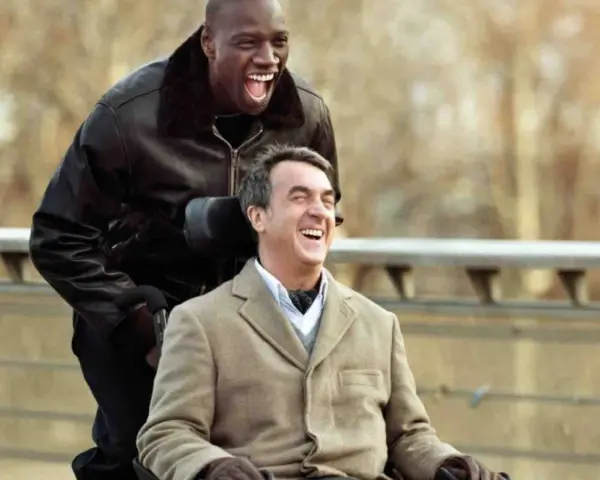 Dwóch mężczyzn, jeden na wózku, śmieje się radośnie. Film "Nietykalni gdzie obejrzeć" to wzruszająca historia przyjaźni.