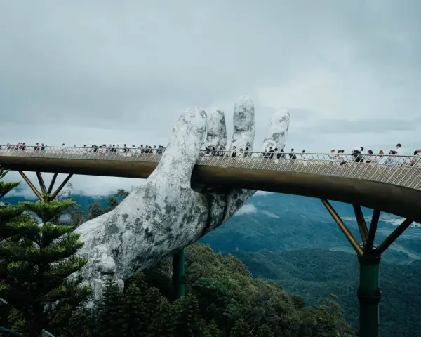 Goldene Brücke in Vietnam, gehalten von einer riesigen Steinhands. Touristen spazieren über die Brücke, die sich durch üppige grüne Berge schlängelt.