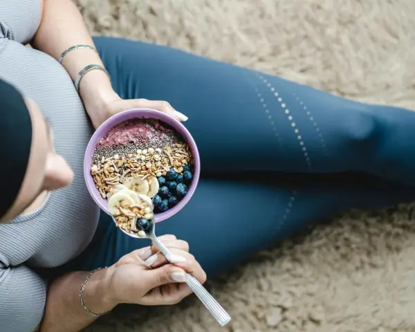 En kvinna äter en näringsrik skål med granola, bär och banan. En bra frukost kan bidra till att uppnå rekommenderat intag av hur mycket protein per dag kvinna.
