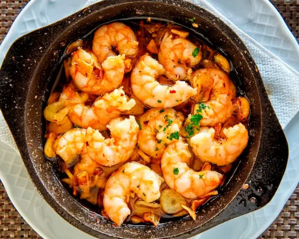 Un plato humeante de langostinos al ajillo, jugosos y dorados, nadando en aceite de oliva con ajo y perejil. ¡Un manjar irresistible!