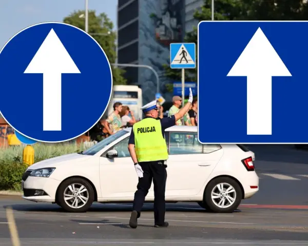 Policjant kieruje ruchem przy znakach droga jednokierunkowa. Biała Skoda czeka na sygnał.