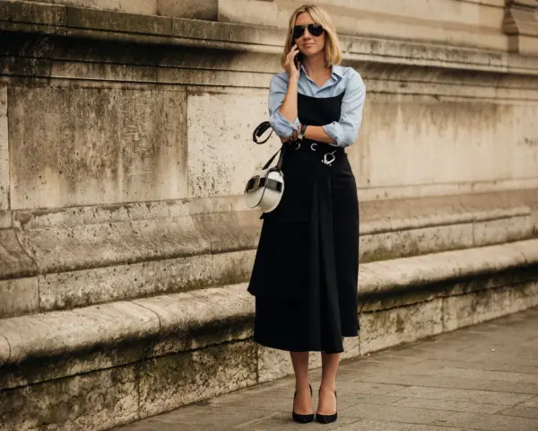 Mujer con un elegante vestido negro sobre una camisa blanca, hablando por teléfono.