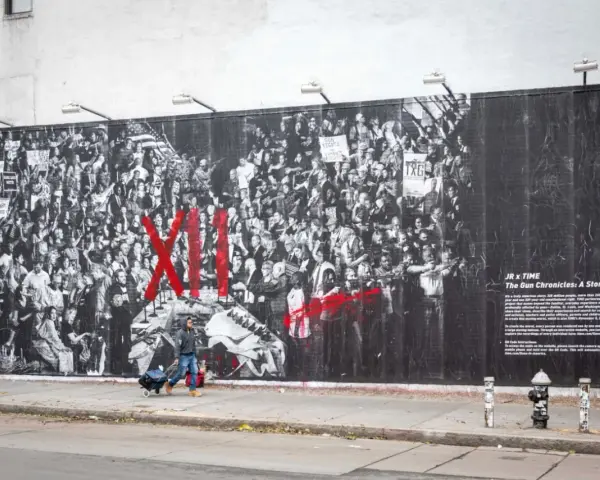 Une fresque murale de street art d'origine, "The Gun Chronicles: A Story of America", par JR x TIME, dépeint une foule en noir et blanc avec des touches de rouge vif.