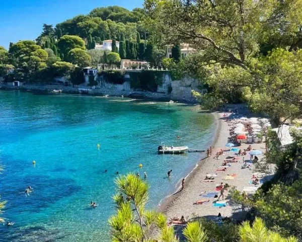 Plage idyllique à Antibes, eaux turquoise, pins parasols et villas sur la falaise. Parfait pour visiter Antibes et se détendre.