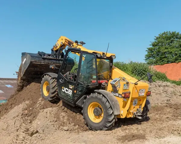 Żółty ładowarka teleskopowa JCB 525-60 z podniesionym wysięgnikiem i łyżką, pracująca na budowie.