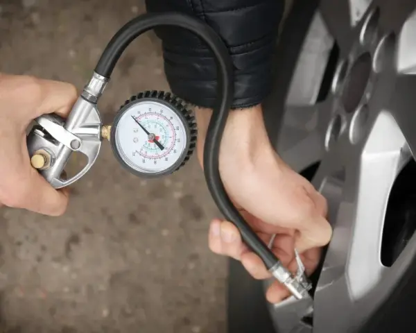 Person prüft den Reifendruck mit einem Manometer. Die warmen Reifen sind wichtig für die Sicherheit.
