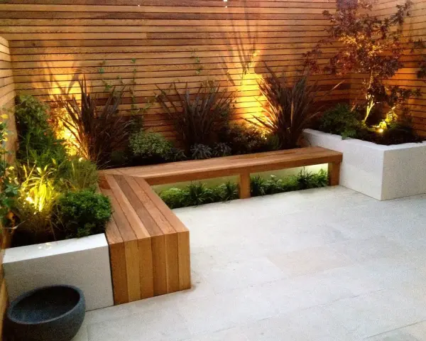 Elegante decoracion patio interior con banco de madera y plantas iluminadas.