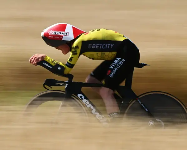 A cyclist in a yellow and black suit, helmet, and aero bars races during the Dauphine cycling event, blurring past the camera.