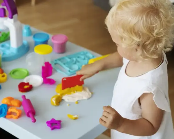 Małe dziecko z blond włosami bawi się masą plastyczną, wspierając swój rozwój sensoryczny.
