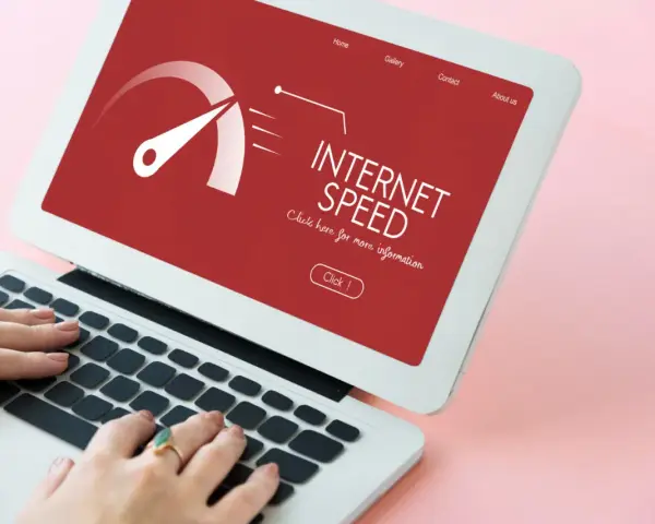 Schermo di un laptop con indicatore di velocità internet su sfondo rosso. Le mani digitano sulla tastiera, frustrati dall'internet lento.