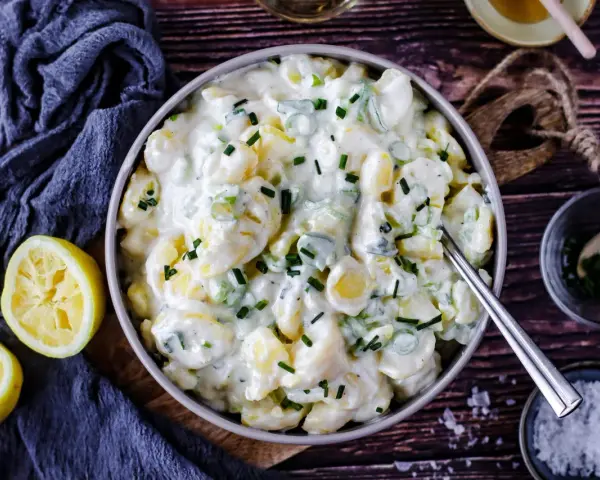 Cremiger Kartoffelsalat mit Joghurt, garniert mit Schnittlauch. Dazu passen frische Zitronenspalten.