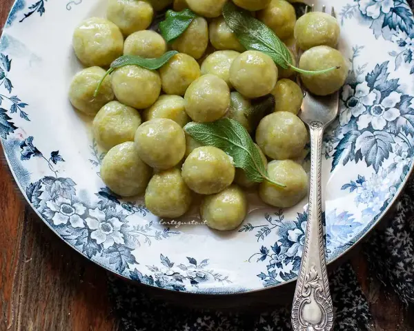 Gnocchi di zucchine morbidi e profumati, guarniti con foglie di salvia fresca su un piatto decorato.
