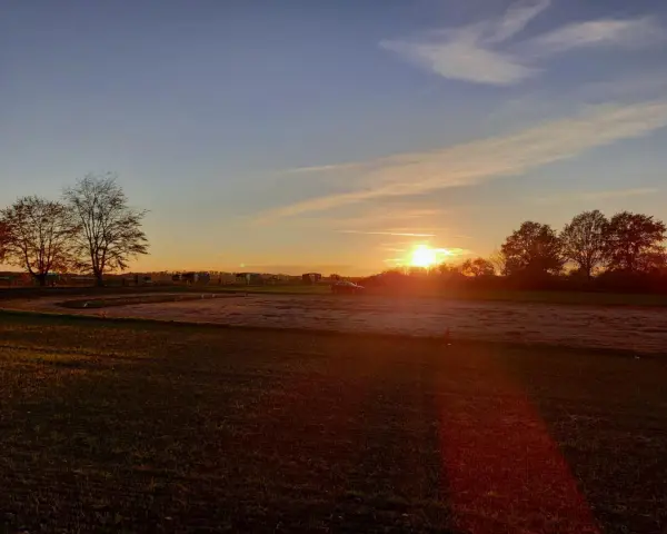 Sonnenuntergang über einem Feld mit Bäumen und einem Auto. "Seid stille und wisset: Ich bin Gott." (Psalm 46:10)