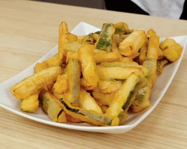 Un piatto bianco pieno di zucchine in pastella dorate e croccanti, pronte per essere gustate.