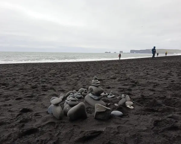 Kamienne stosy na czarnej plaży Islandii, z widokiem na ocean i skaliste wybrzeże.