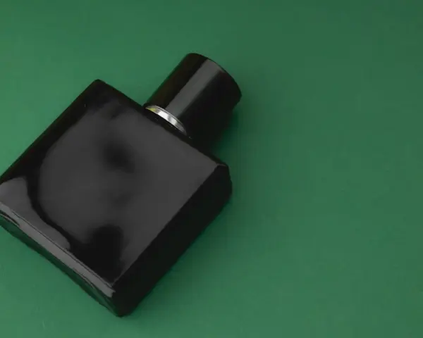 Czarna, elegancka butelka perfum z nutą wetiwery na zielonym tle.