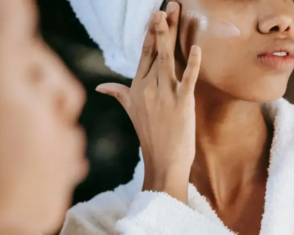 Une femme applique une crème hydratante sur sa joue, un geste essentiel pour savoir comment bien hydrater son visage et obtenir une peau éclatante.