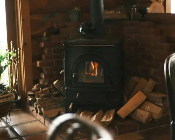 Poêle à bois avec arrivée d'air extérieur, crépitant joyeusement dans un coin cosy, entouré de bois prêt à chauffer.
