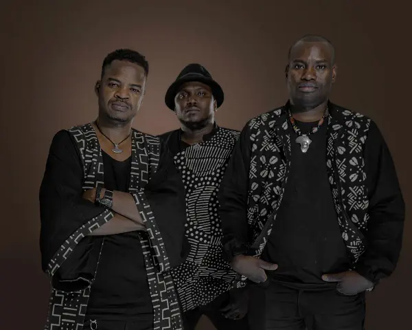 Trois hommes en tenue traditionnelle africaine, évoquant l'ancêtre du blues, posent avec assurance.