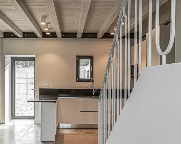 Interno moderno con travi a vista in legno, illuminazione led soffusa e una scala bianca.