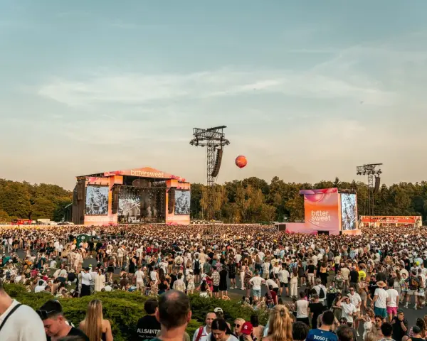 Tłum ludzi na festiwalu bittersweet, dwie sceny, ekrany z grafikami i pomarańczowy balon na niebie.