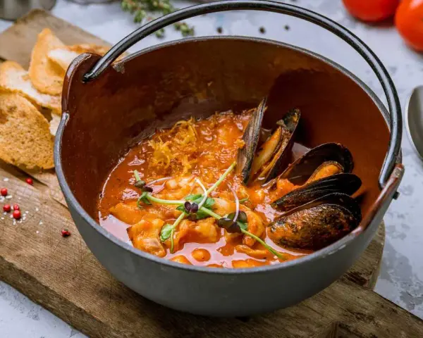 Un delicioso suquet de peix, con mejillones y gambas en una cazuela de barro, acompañado de tostadas.