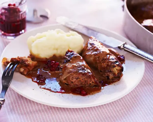 Kåldolmar recept: två saftiga kåldolmar med potatismos och lingonsylt, serverade med en mustig sås.