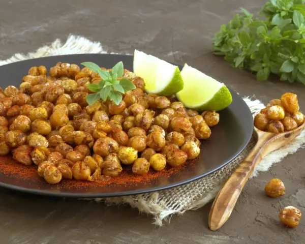 Ceci croccanti al forno, conditi con paprika e guarniti con basilico fresco e spicchi di lime, invitano a uno snack salutare e gustoso.
