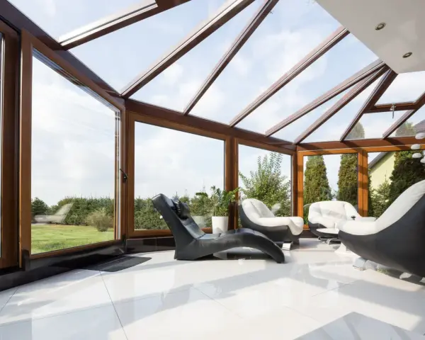 Nowoczesna oranżeria z drewnianymi okna ze szprosami, wygodnymi fotelami i widokiem na ogród.