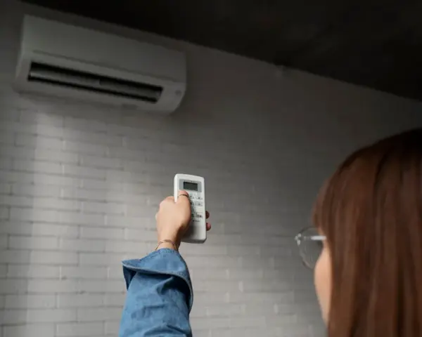 Persona ajusta control remoto de aire acondicionado, pensando en el consumo de la bomba de calor.