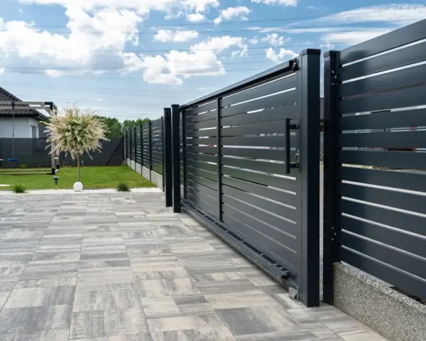 Solidny fundament pod bramę przesuwną zapewnia jej stabilność i płynne działanie. Nowoczesna, ciemnoszara brama z poziomymi lamelami.