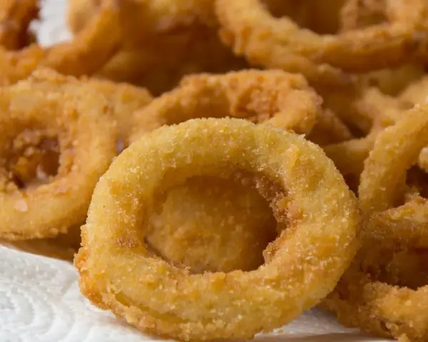 Knusprige zwiebelringe in der pfanne, goldbraun und perfekt frittiert, liegen auf einem weißen Küchentuch.